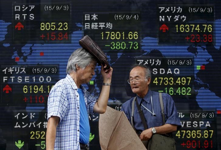 © Reuters. A pedestrian taking shelter from rain walks past an electronic board showing the stock market indices of various countries outside a brokerage in Tokyo