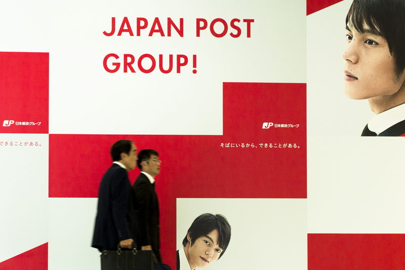 © Reuters. Men walk past an advertising poster at the head office of Japan Post in Tokyo 