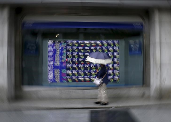 © Reuters. A woman holding an umbrella looks at an electronic stock quotation board outside a brokerage in Tokyo