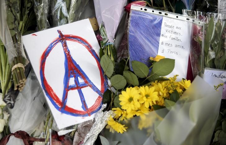 © Reuters. Varias personas dejan flores, dibujos y mensajes en recuerdo de las víctimas de los ataques de París