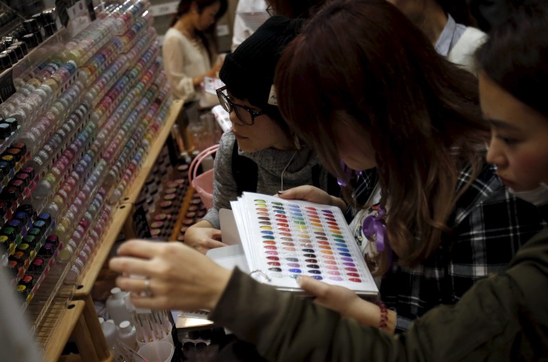 © Reuters. Shoppers look at various colors of manicure displayed at an exhibition and sale during Tokyo Nail Expo 2015 in Tokyo