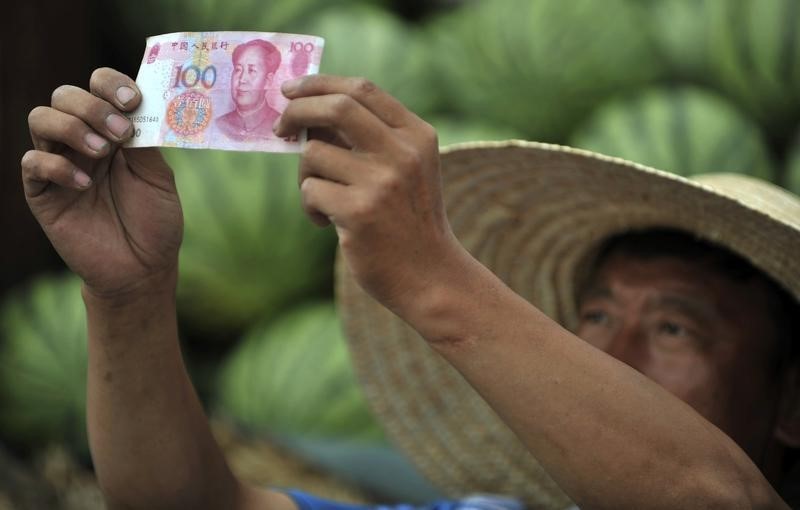 © Reuters. A watermelon vendor looks at a yuan banknotes at a market in Shenyang