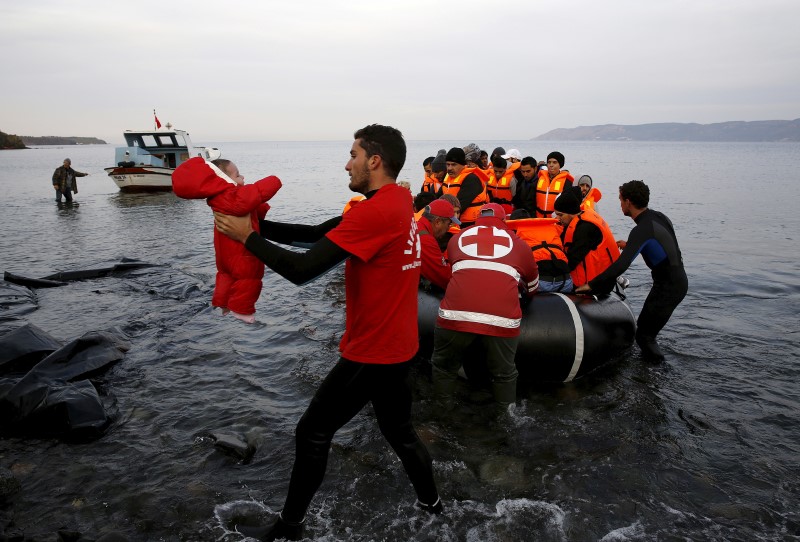 © Reuters. A Red Cross volunteer carries a refugee baby at a beach on the Greek island of Lesbos