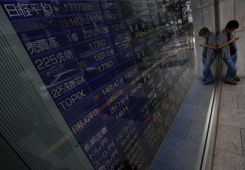 © Reuters. A pedestrian looks at his mobile phone stands in front of an electronic board showing various stock prices outside a brokerage in Tokyo