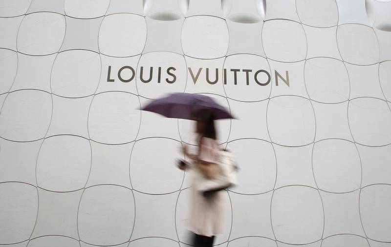 © Reuters. A woman holding umbrella walks past a Louis Vuitton logo outside its branch store at Ginza shopping street in Tokyo