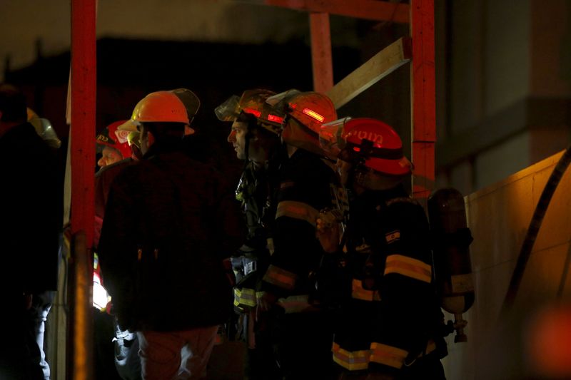 © Reuters. Israeli fire-fighters stand at the entrance to an office building where the offices of B'Tselem is located, in Jerusalem