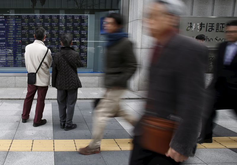 © Reuters. Pedestrians look at an electronic board showing the various stock prices outside a brokerage in Tokyo