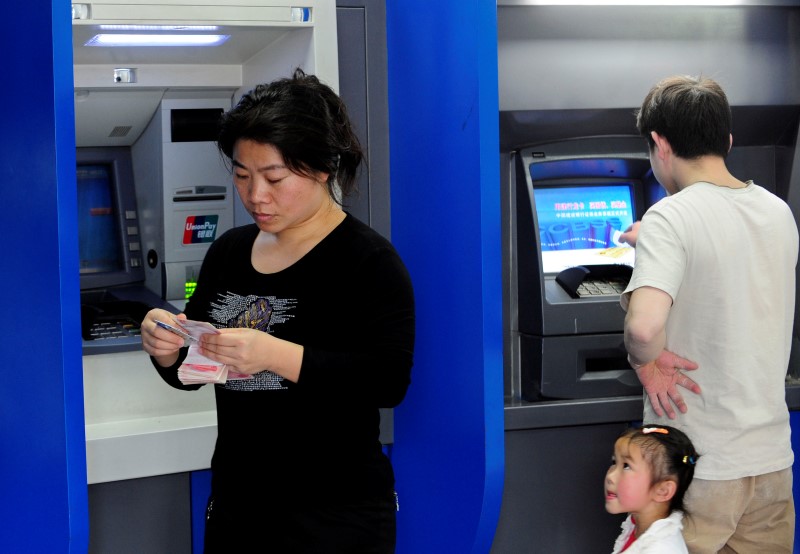 © Reuters. A woman counts yuan banknotes after withdrawing cash from an automatic teller machine (ATM) in Hefei