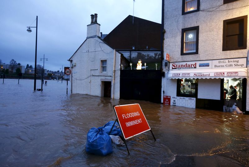 © Reuters. A flood warning sign is pictured in front of local businesses on a flooded street in Dumfries