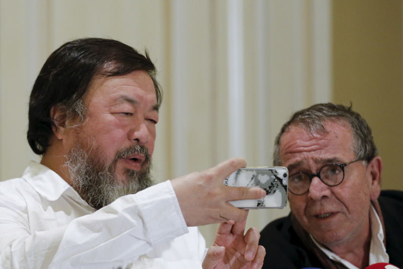 © Reuters. Chinese artist Ai Weiwei takes a picture with his phone next to Greek Migration Minister Mouzalas before a news conference in Athens