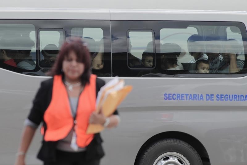 © Reuters. Woman walks in front of a bus filled with deportees at the Soto Cano military base in Comayagua