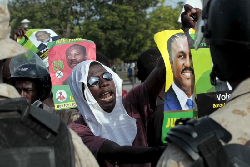 © Reuters. A supporter of presidential candidate Jude Celestin shows a poster of Celestin to a national police officer during a demonstration against the results of the presidential elections released last week in Port-au-Prince