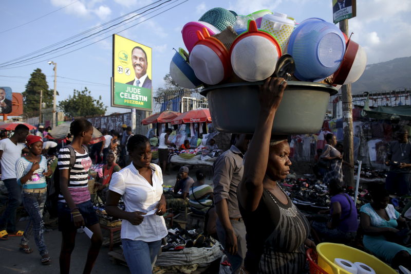 © Reuters. Residents walk next to an electoral sign of presidential candidate Jude Celestin in Port-au-Prince, Haiti