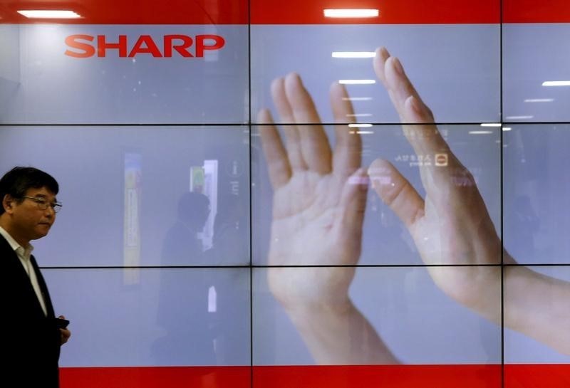 © Reuters. A man walks past display showing a logo of Sharp Corp in Tokyo