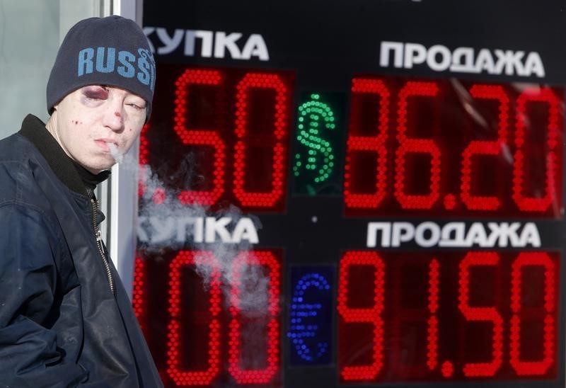 © Reuters. A man smokes near a board showing currency exchange rates of the U.S. dollar and euro against the rouble in Moscow