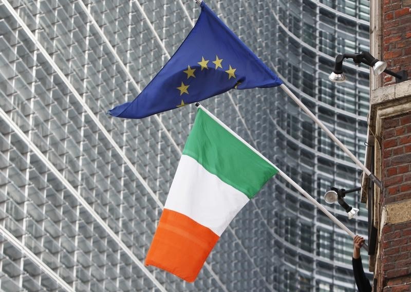 © Reuters. A man adjusts an Irish flag as it flies next to a European Union flag near the EU Commission headquarters in Brussels
