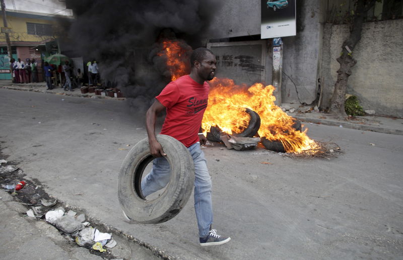 © Reuters. A protester carries a tire as he passes next to a burning barricade during a demonstration against the electoral process in Port-au-Prince, Haiti