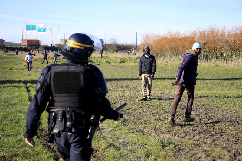 © Reuters. A French riot policeman stops migrants in a field near Calais, France, as migrants gather in the hopes of attempting to board lorries and making their way across the Channel to Britain