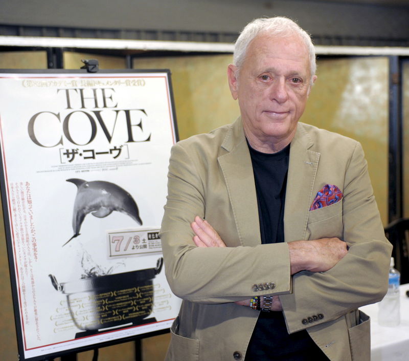 © Reuters. Ric O'Barry, a U.S. dolphin conservationist who appeared in the Oscar-winning documentary "The Cove", poses with a poster of his film before a news conference in Osaka