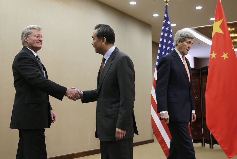 © Reuters. U.S. Secretary of State John Kerry walks past as Chinese Foreign Minister Wang Yi shakes hands with U.S. Ambassador to China Max Baucus before their bilateral meeting at the Ministry of Foreign Affairs in Beijing
