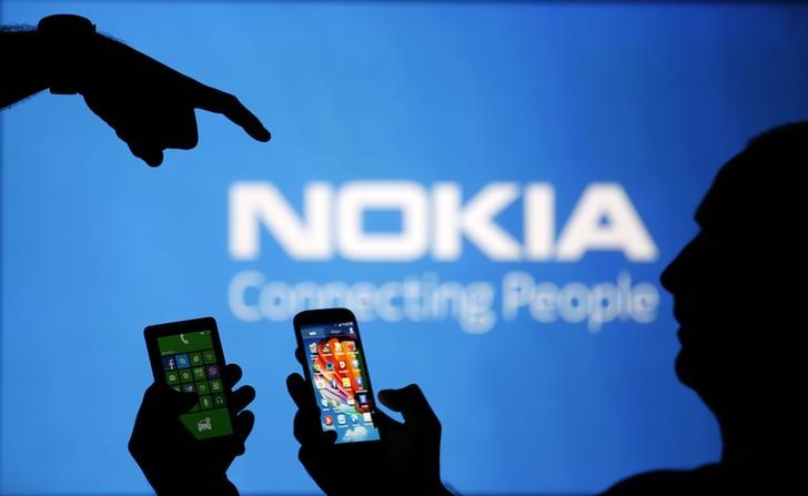 © Reuters. Men are silhouetted against a video screen with an Nokia logo as he poses with an Nokia Lumia 820 and Samsung S4 smartphones in this photo illustration taken in the central Bosnian town of Zenica