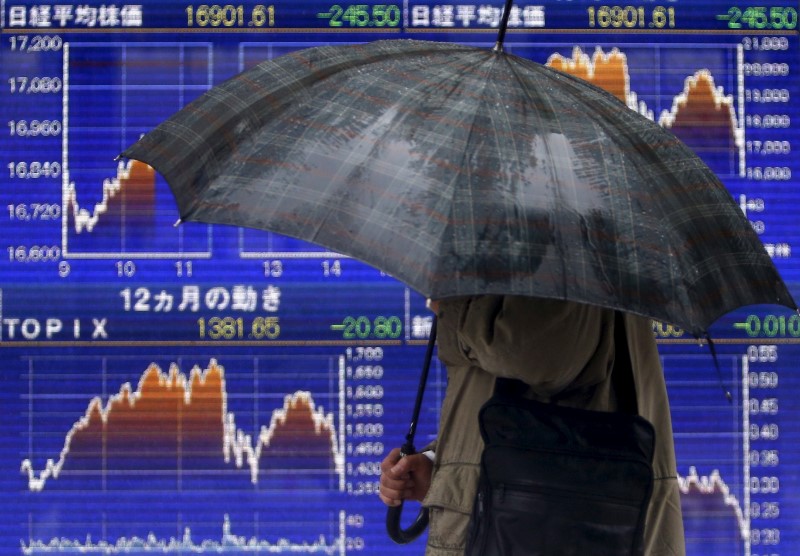 © Reuters. A pedestrian holding an umbrella walks past an electronic board showing the graphs of the recent fluctuations of Japan's Nikkei average outside a brokerage in Tokyo