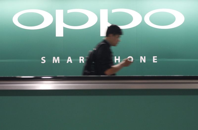 © Reuters. File photo of a commuter using his mobile phone passing an advertisement of Chinese smartphone maker Oppo at a train station in Singapore
