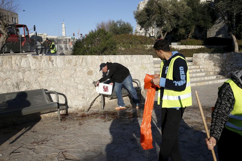 © Reuters. A man pours water over blood stains at the scene where three Palestinians were shot dead by Israeli police after carrying out what Israeli police spokesman said, a shooting and stabbing attack outside Damascus gate to Jerusalem's old city