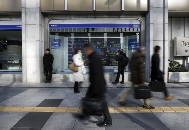 © Reuters. A pedestrian looks an electronic board showing the stock market indices of various countries outside a brokerage in Tokyo