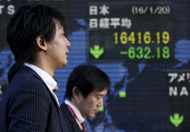 © Reuters. Men walk past an electronic board showing Japan's Nikkei average outside a brokerage in Tokyo