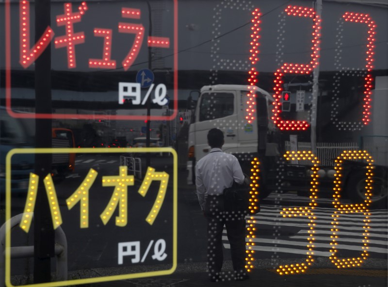 © Reuters. A man and vehicles are reflected in a price display at a gas station in Tokyo