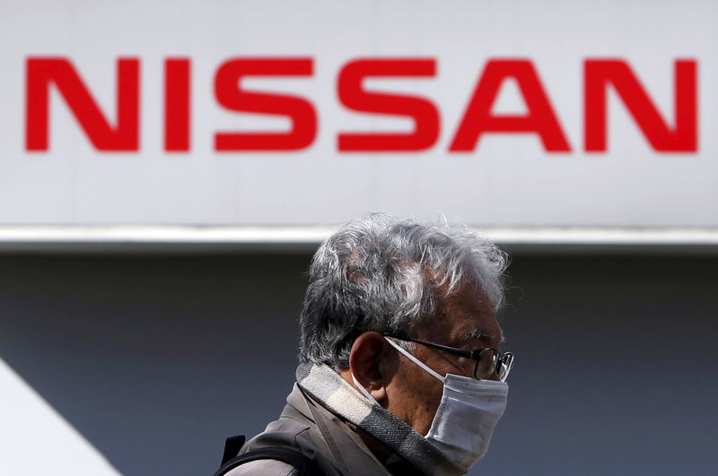 © Reuters. A man wearing a mask walks under a logo of Nissan Motor Co. outside the company's dealership in Tokyo