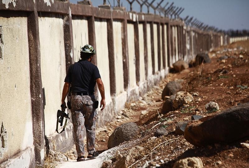 © Reuters. A Free Syrian Army fighter carries his weapon as he walks along the fence of the Menagh airport which, according to the FSA, is partially controlled by Syrian regime forces in Aleppo's countryside