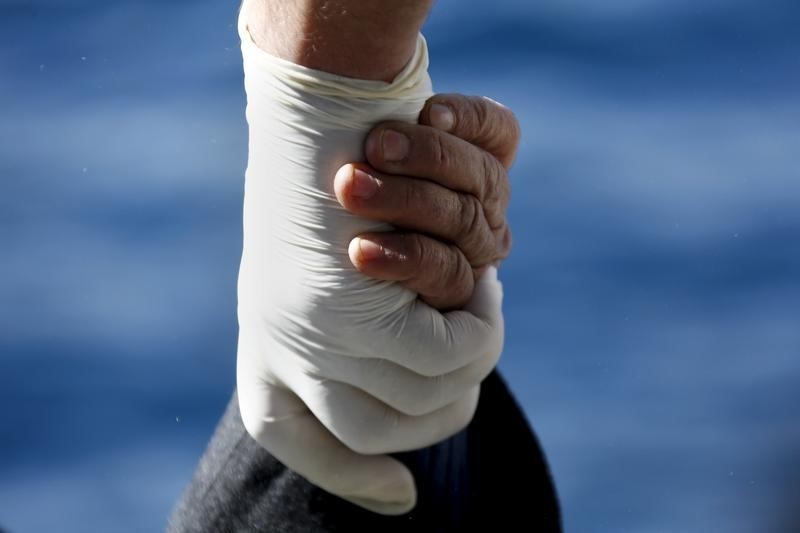 © Reuters. A migrant holds the hand of a Greek Coast Guard officer, while being retrieved from a dinghy carrying refugees and migrants aboard the Ayios Efstratios Coast Guard vessel, during a rescue operation at open sea 