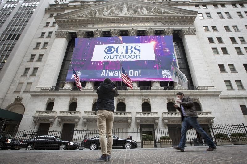 © Reuters. A man takes a photo of a CBS Outdoor banner displayed on the facade of the New York Stock Exchange