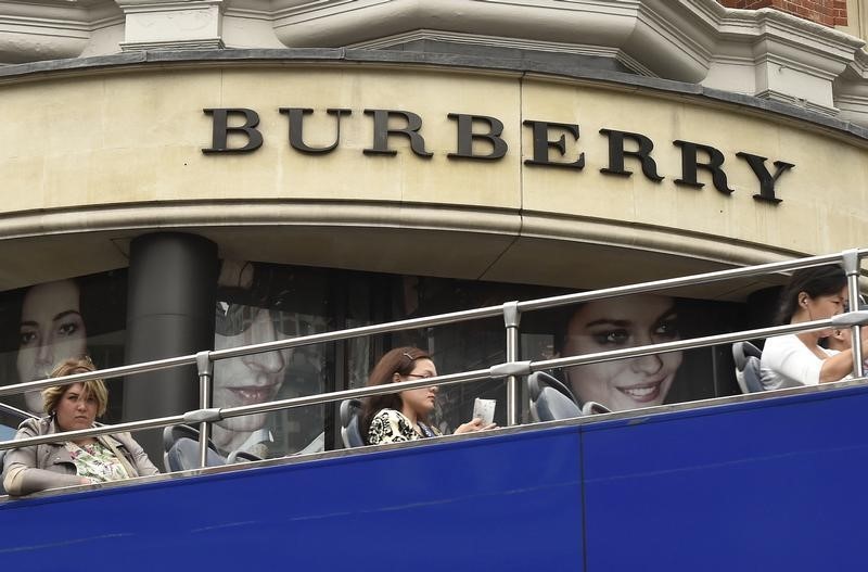 © Reuters. Visitors on an open-top tour bus drive past a Burberry store in central London