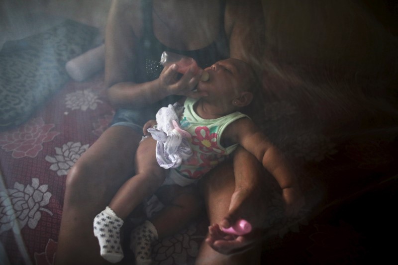 © Reuters. Vanessa, feeds her daughter Valentina, who is 5-months old and born with microcephaly, with a bottle under a mosquito net, inside their house in Jaboatao