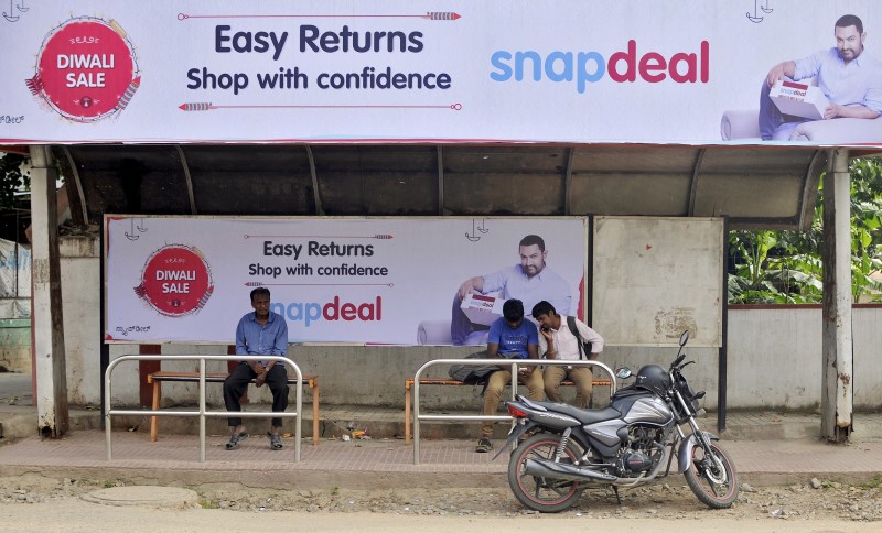 © Reuters. Commuters sit at a bus stop adorned with an advertisement of Indian online marketplace Snapdeal featuring Bollywood actor Aamir Khan, in Bengaluru, India