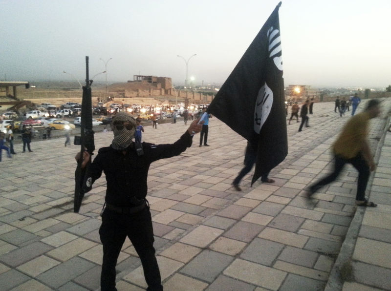 © Reuters. A fighter of the ISIL holds a flag and a weapon on a street in Mosul