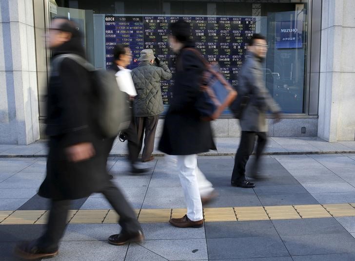 © Reuters. Man looks at an electronic stock quotation board as passers-by walk past, outside a brokerage in Tokyo