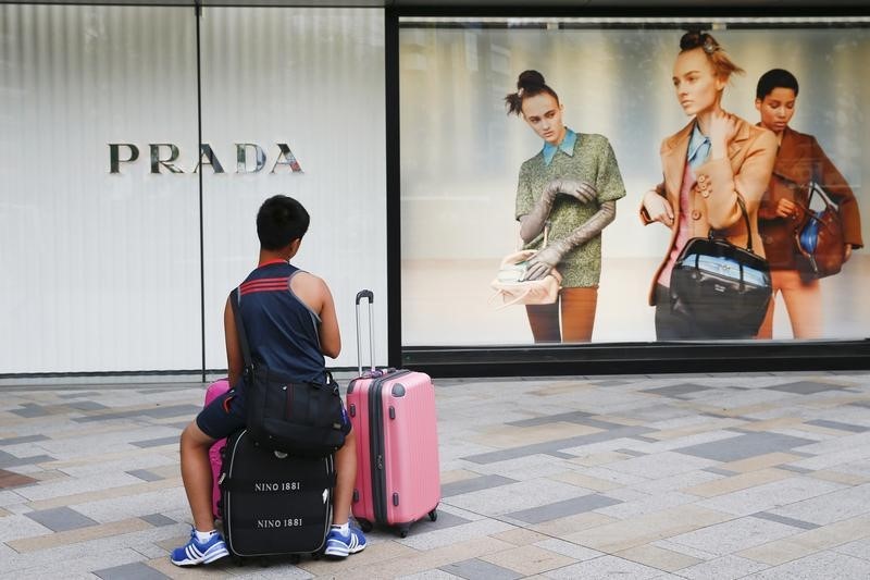 © Reuters. Man sits on suitcases in front of an advertising window of luxury goods retailer Prada in Tokyo