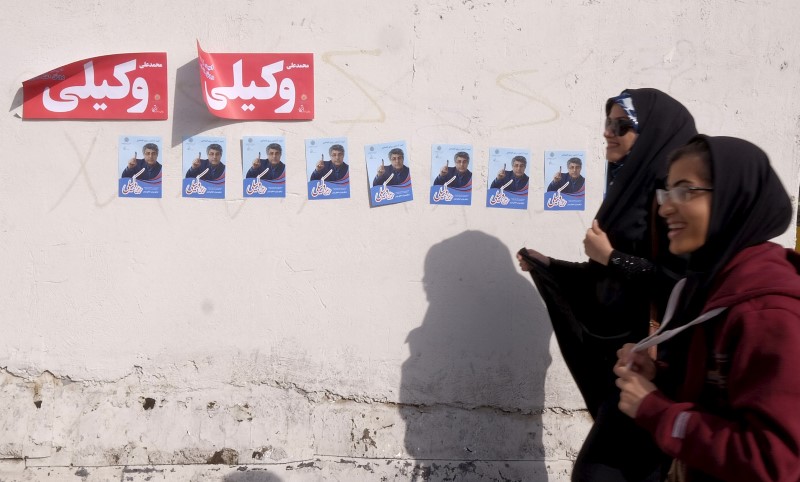 © Reuters. Women walk past electoral posters for the upcoming parliamentary elections in central Tehran 