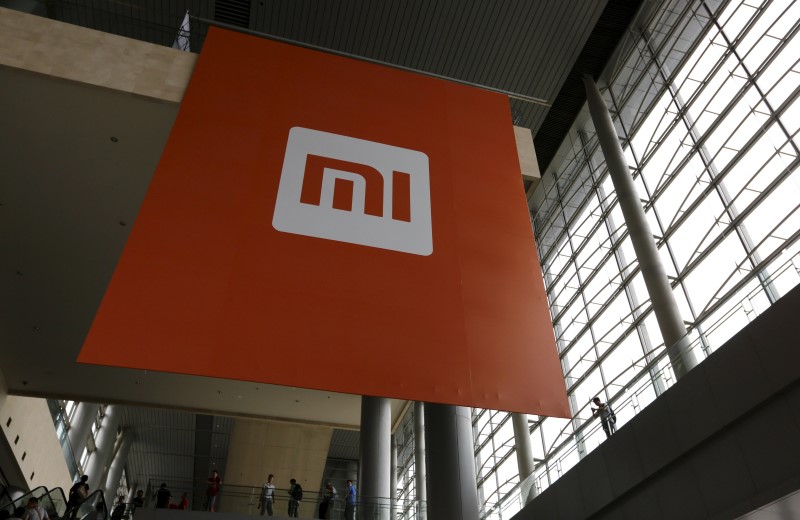 © Reuters. File picture of people standing near a logo of Xiaomi ahead of the launching ceremony of Xiaomi Phone 4, in Beijing