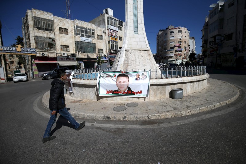 © Reuters. Palestinian youth walks past a poster depicting Palestinian journalist Mohammad al-Qiq, who was detained by Israeli forces in November and is on the 86th day of a hunger strike in a hospital in northern Israel, in Ramallah