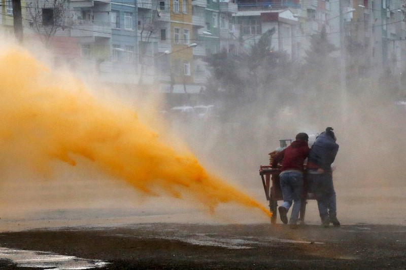 © Reuters. Street vendors take cover as Turkish riot police use a water cannon to disperse Kurdish demonstrators during a protest against the curfew in Sur district, in the southeastern city of Diyarbakir