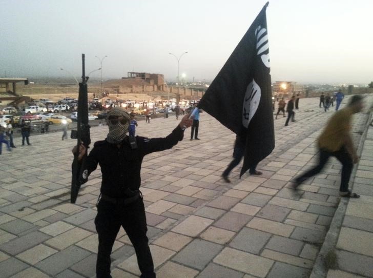 © Reuters. A fighter of the ISIL holds a flag and a weapon on a street in Mosul