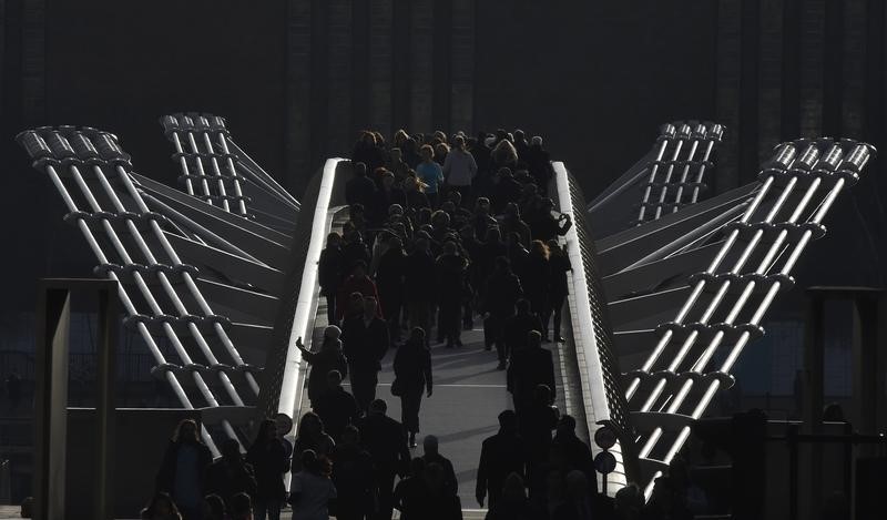 © Reuters. Workers are seen walking over the Millennium footbridge during the lunch hour in the City of London, in Britain