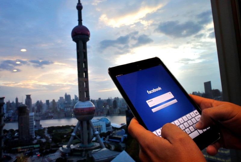 © Reuters. Photo illustration of man holding iPad with a Facebook application in an office building at the Pudong financial district in Shanghai