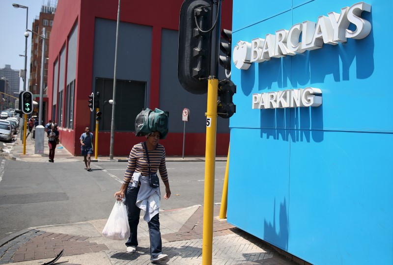 © Reuters. A women carries her belongings on her head as she walks past a Barclays logo in Johannesburg