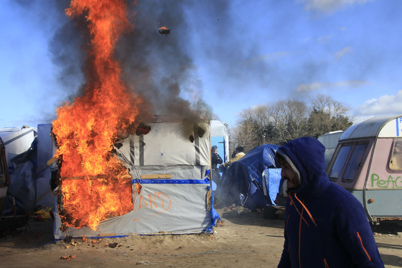 © Reuters. Smoke and flames rise from a burning makeshift shelter set ablaze to protest the partial dismantlement of the camp for migrants called the "jungle", in Calais